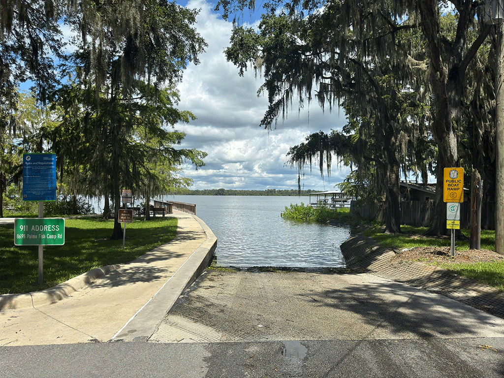A concrete boat ramp leading into the Intracoastal, with trees and signs on either side