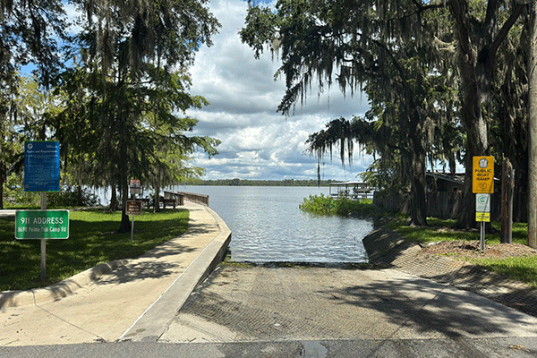 A concrete boat ramp leading into the Intracoastal, with trees and signs on either side.