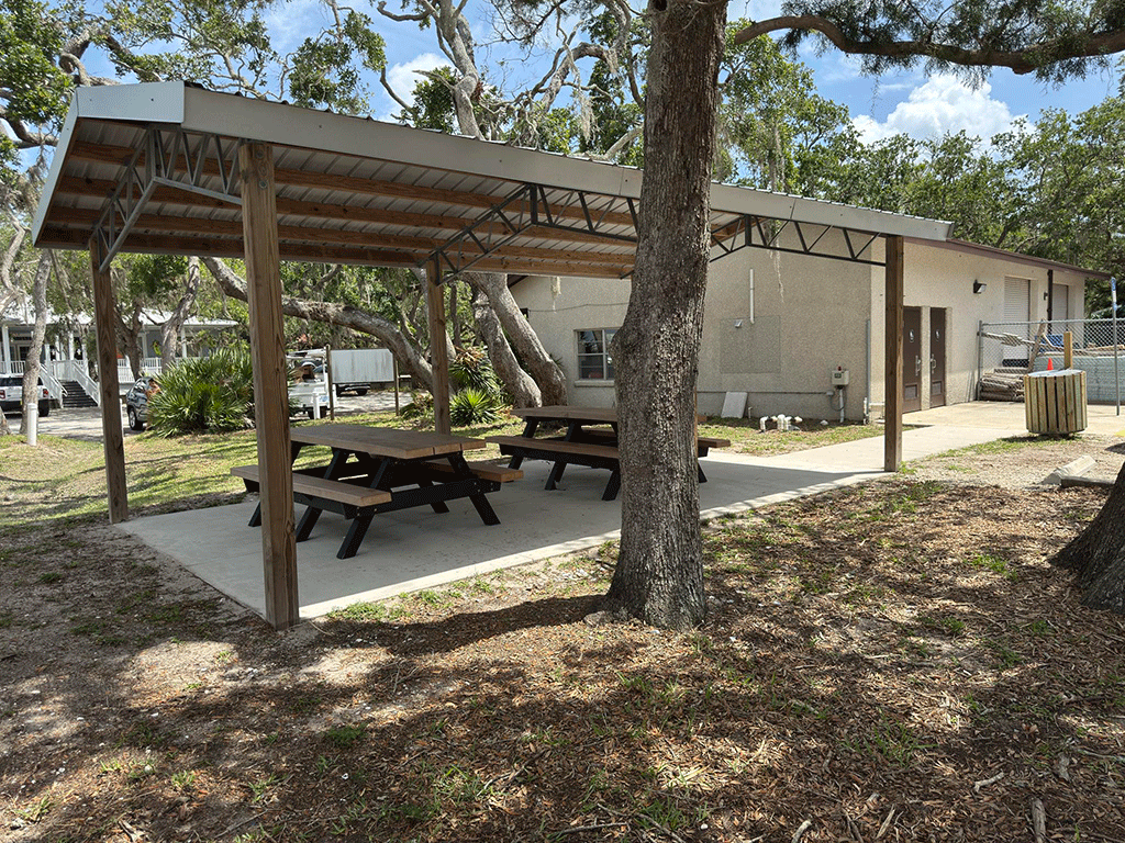 A covered pavilion with picnic tables in front of a public bathroom facility.