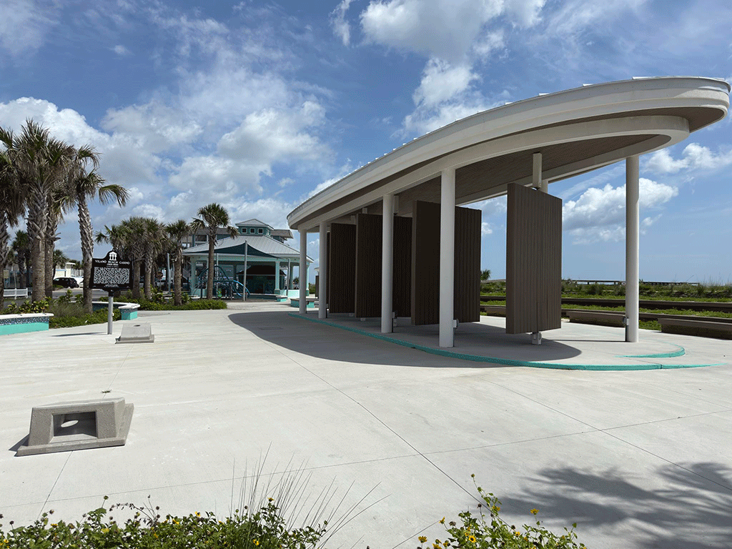 A concrete amphitheater by a beach, with cornhole to one side and a play area and pavilion in the background.