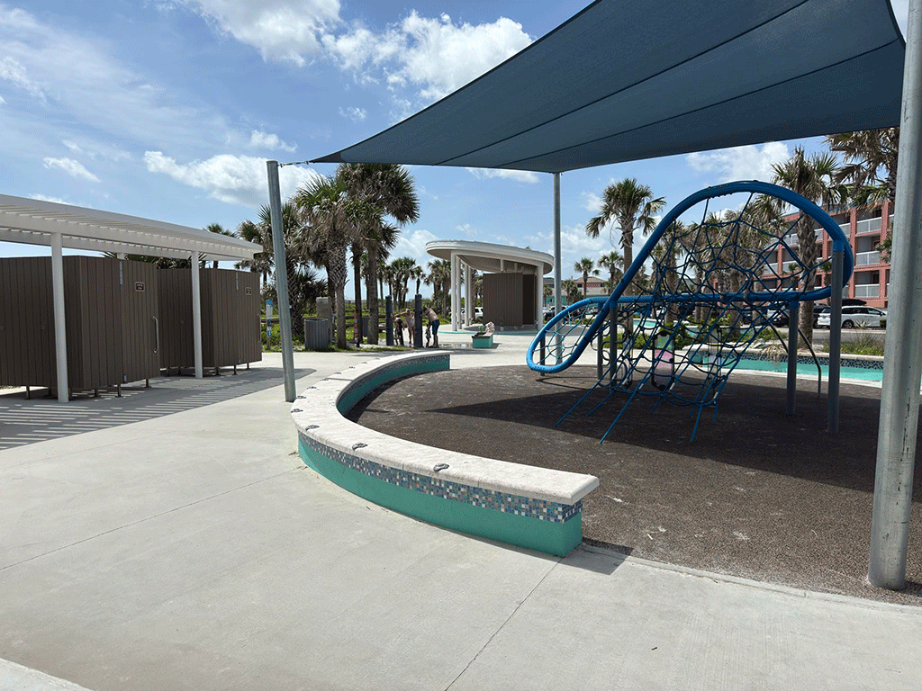 A covered kids’ play area and beach changing rooms, with a family using beach showers in the background
