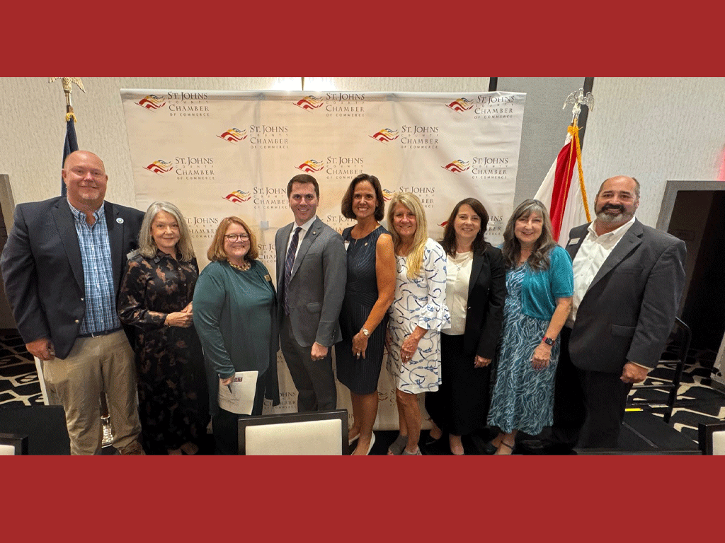 People stand posed for a photo in front of a St, Johns County Chamber of Commerce background.