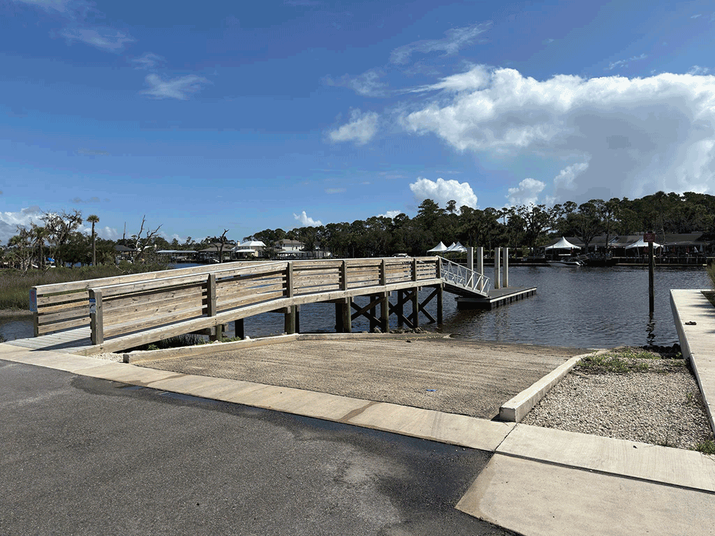 A boat ramp next to a wooden dock, with boats and a restaurant in the background