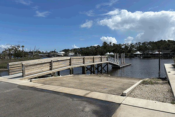 A boat ramp next to a wooden dock, with boats and a restaurant in the background