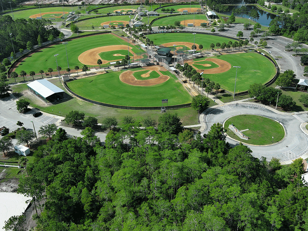 An aerial view of a sports complex with multiple baseball and softball fields, along with batting cages and parking spaces.