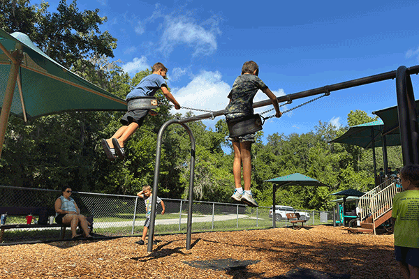 Two boys are seen in midair on a playground swing set.