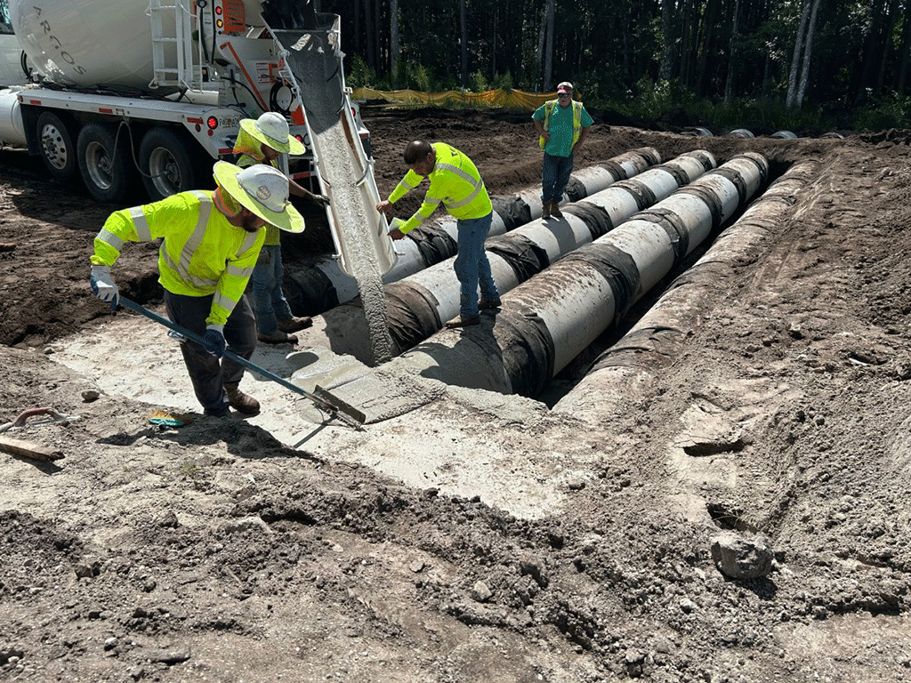 Construction crew pouring cement around in in-ground pipes.