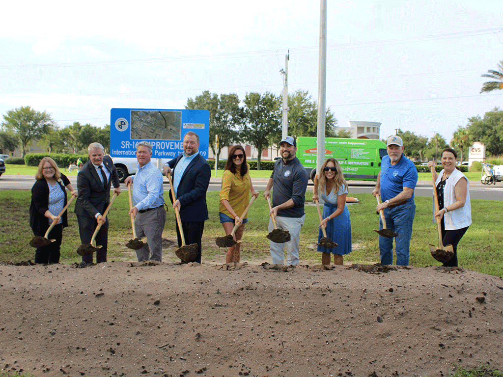 Commissioners and others stand with golden shovels in front of dirt mounds.