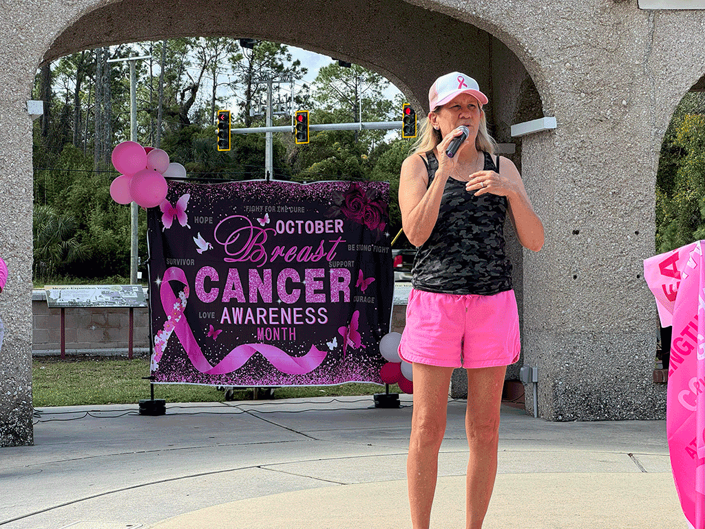 Commissioner Joseph speaks into a microphone in front of a banner that says "October Breast Cancer Awareness Month"