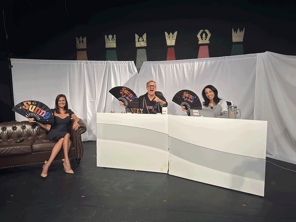 Commissioner Sarah Arnold sits on a stage with two others holding fans that say "SUNNY"