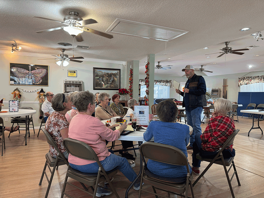 Commissioner Murphy stands speaking to groups seated at round tables.