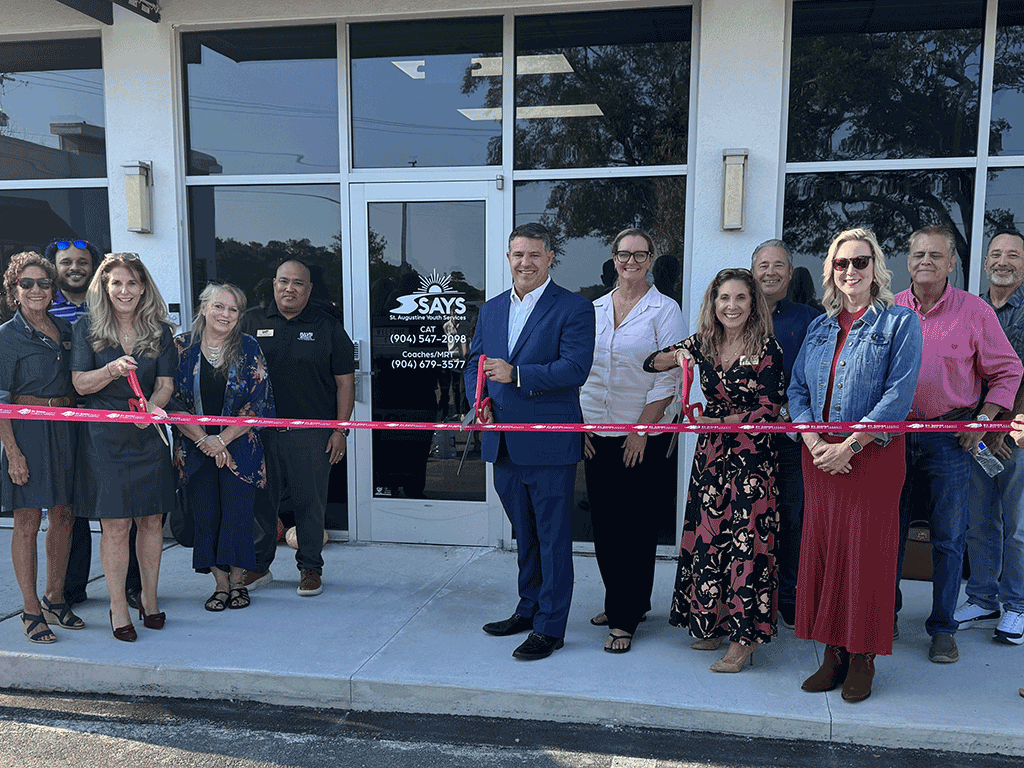 Commissioner Taylor stands with others holding giant scissors ready to cut a red ribbon in front of the St. Augustine Youth Services building.