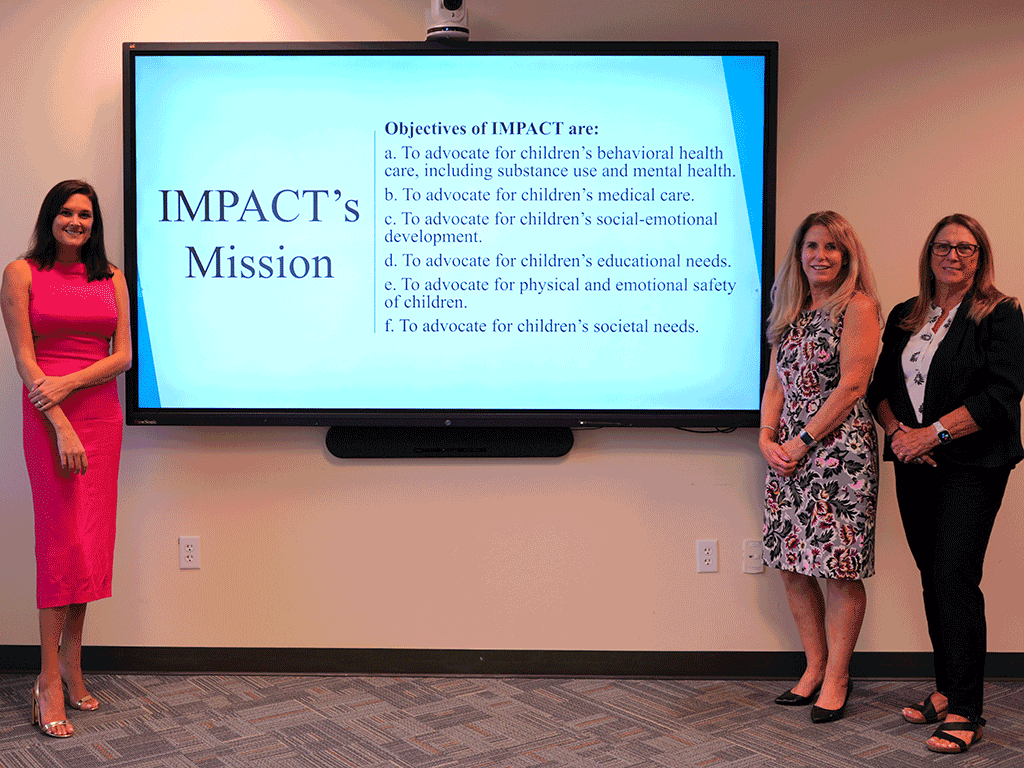 Commissioner Sarah Arnold, Co-Chair Schuyler Siefker, and Co-Chair-Patti Greenough stand in front of the IMPACT Mission Statement
