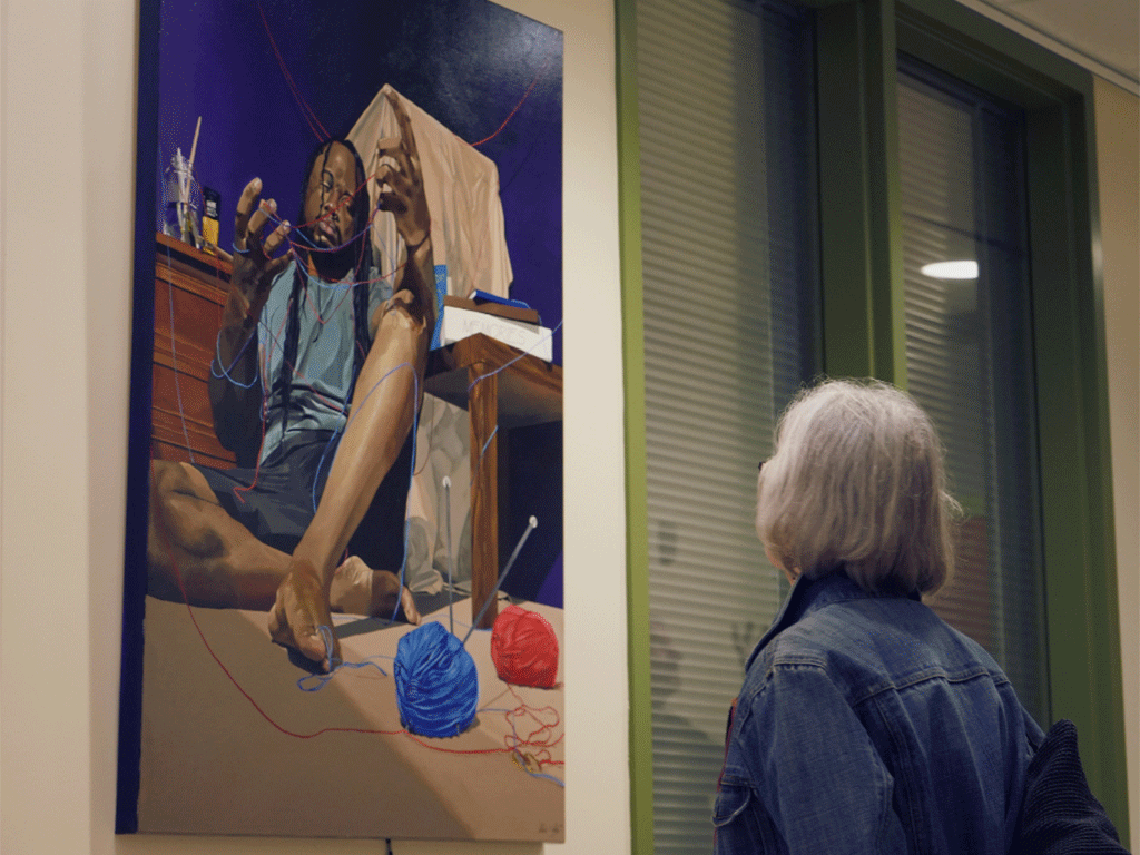 Woman admiring a colorful painting of man twisting yarn through his fingers