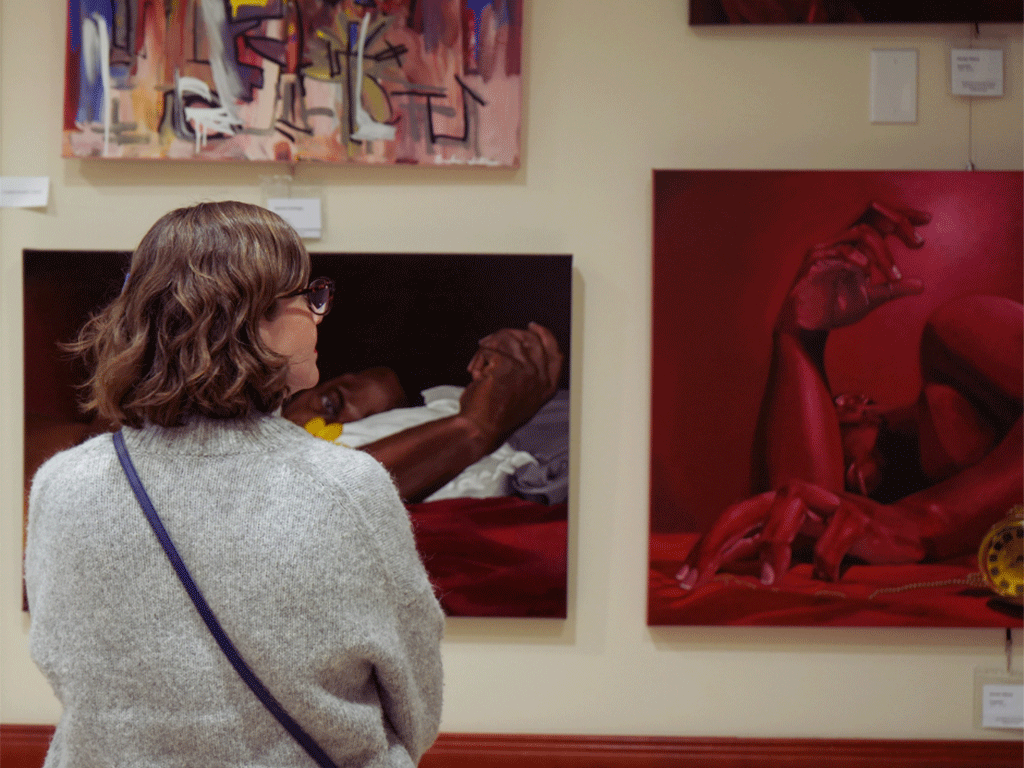 Woman admiring several colorful paintings at art show