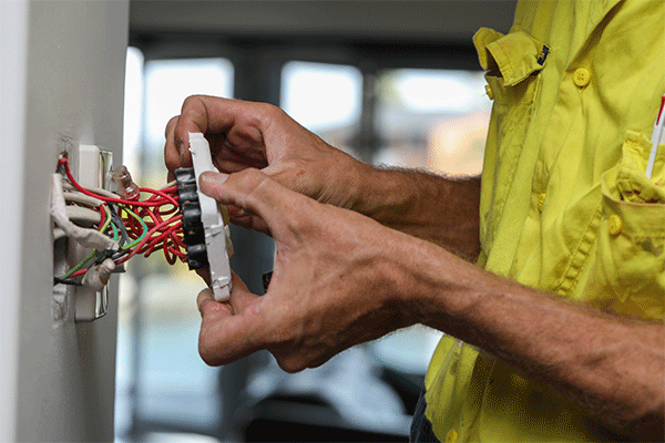 A close up of an electrician working on a light switch at a clients home.