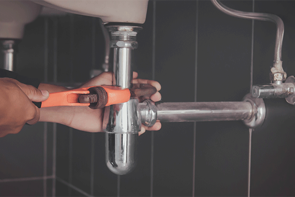 two hands holding a pipe wrench on a drain pipe under sink