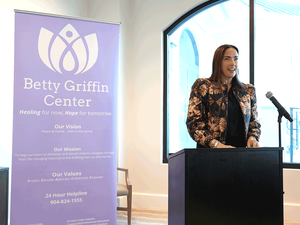 Kristen Martino speaks into microphone at podium with Betty Griffin Center signage behind her