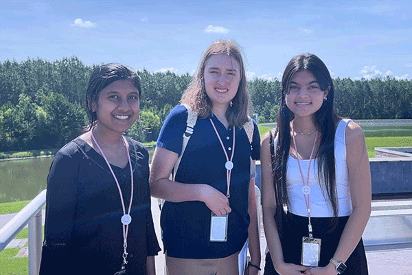 Three students stand outside wearing badges.