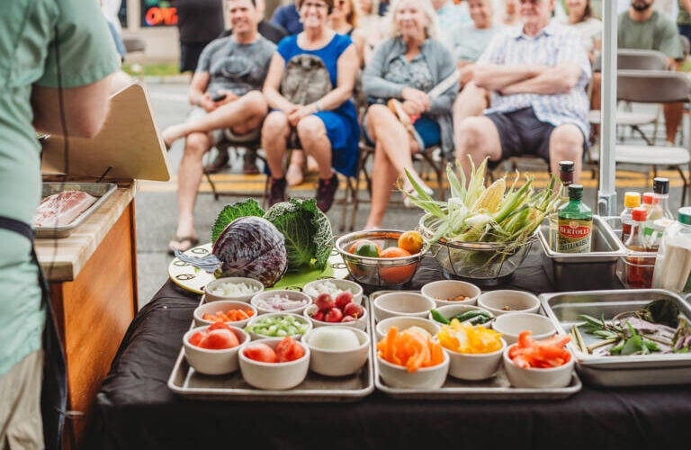Ingredients on a table for a cabbage dish with a presenter next to them and an audience in front