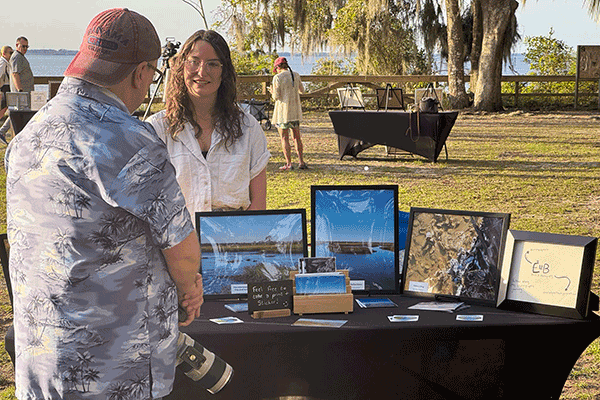 A man with a camera talks to a woman at an outdoor stall displaying her nature photography