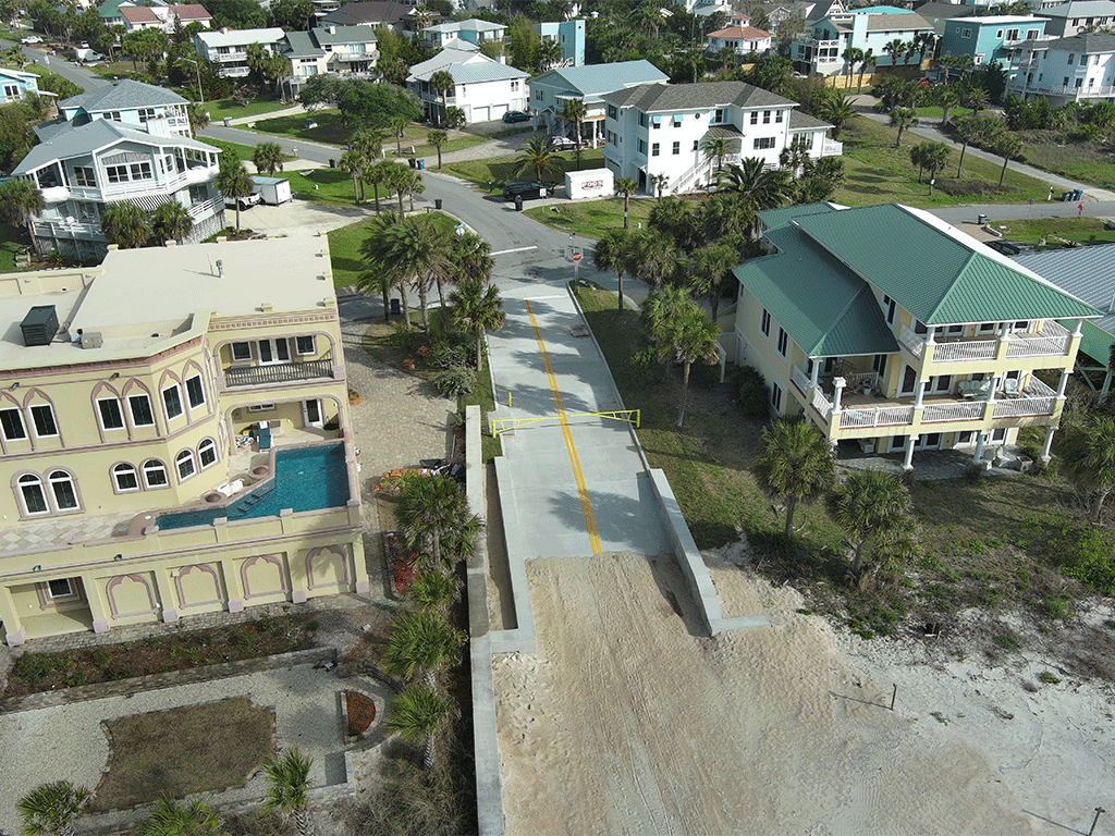 A newly paved vehicular beach access with a gate and toll booth in between two buildings.