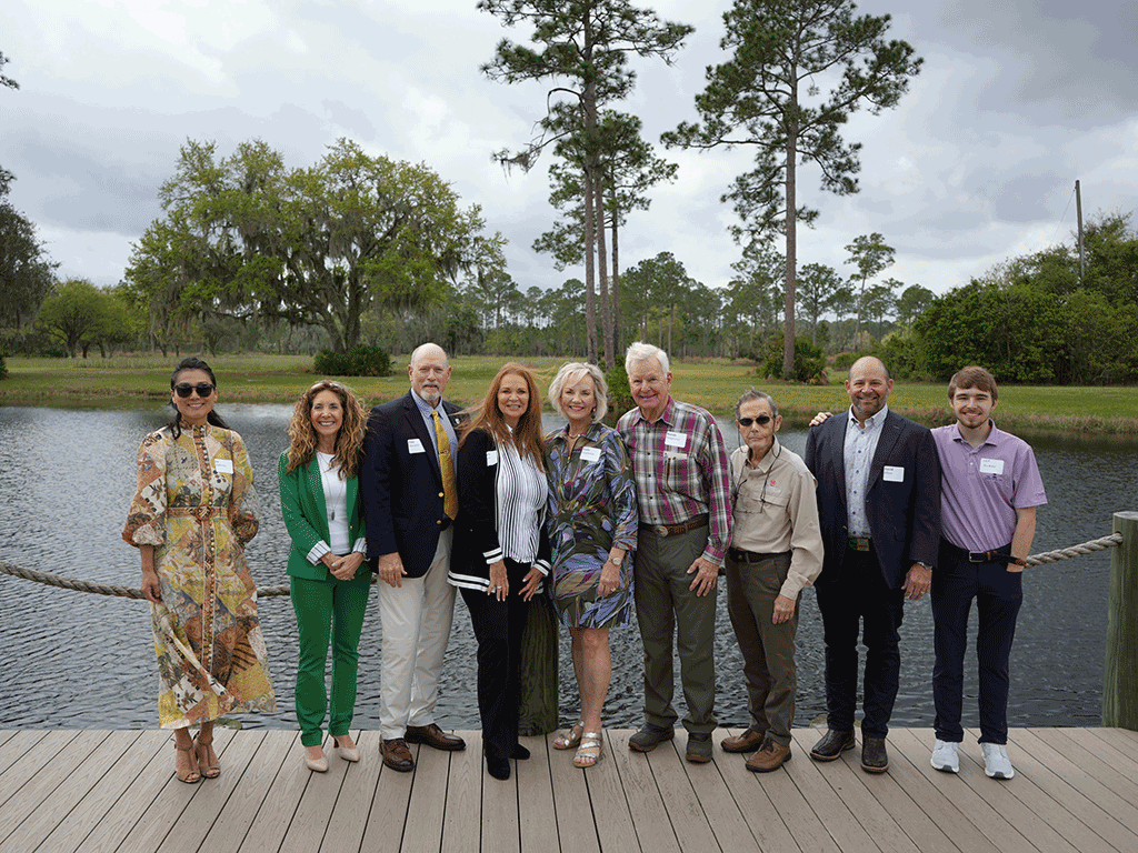 Commissioner Taylor, Commissioner Murphy, County Administrator Joy Andrews, and others stand in front of a lake