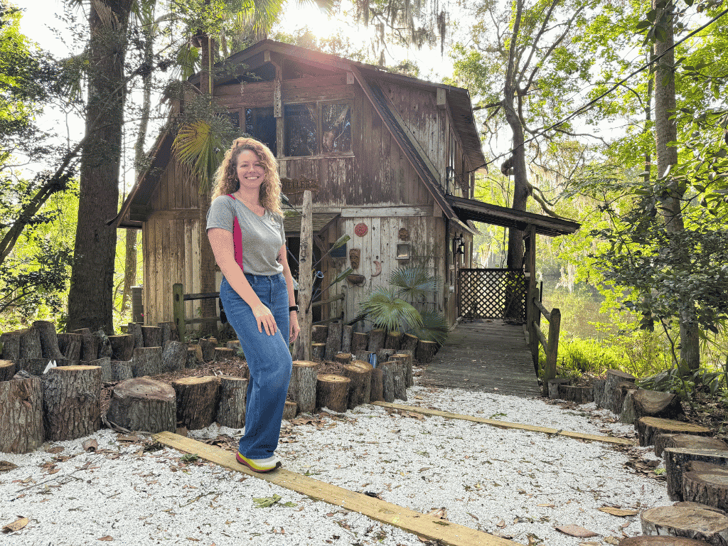 Individual standing in front of a cabin with sun shining through the trees
