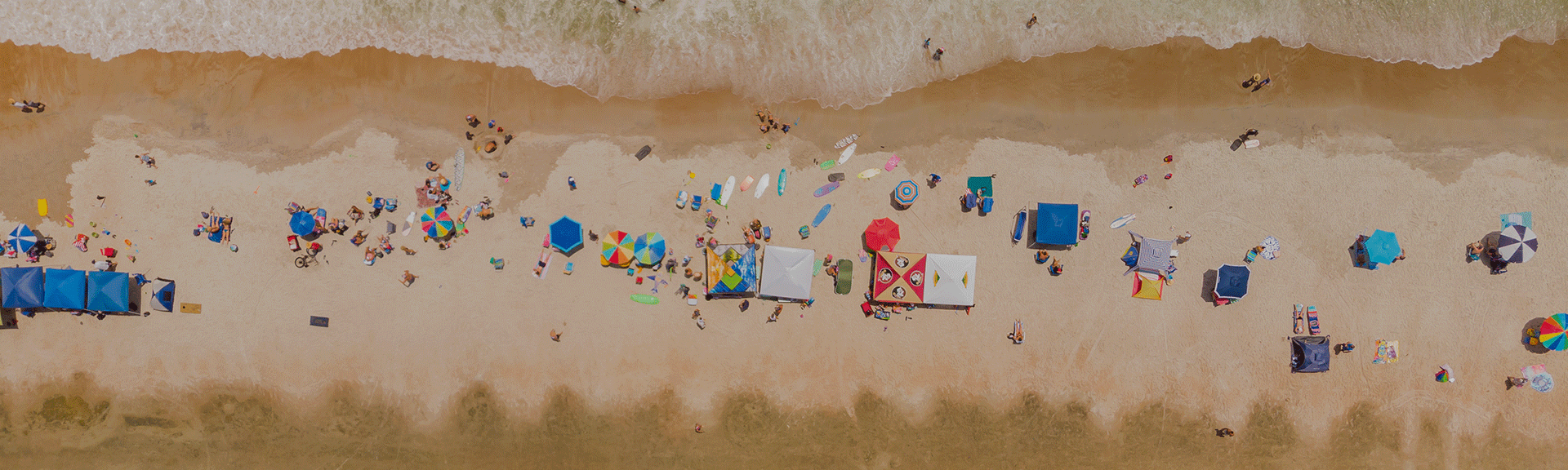 aerial view of beachgoers with canopies and surfboards