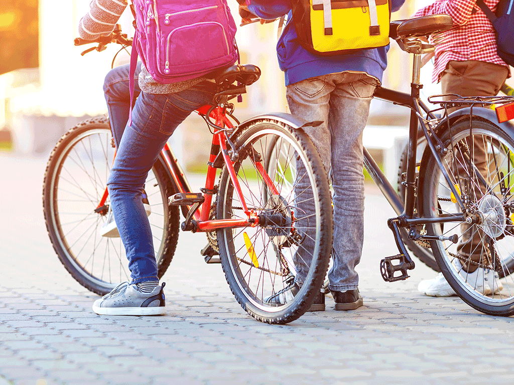 Children with rucksacks riding on bikes in the park near school