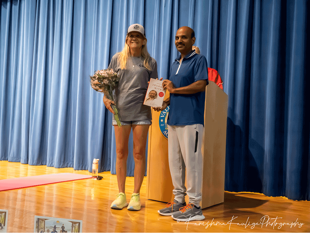Commissioner Joseph stands with flowers on a stage with Dr. Saji Gopalan