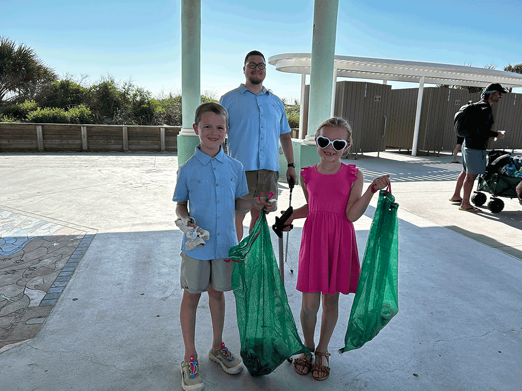 Two children hold bags of trash on a beach pavillion