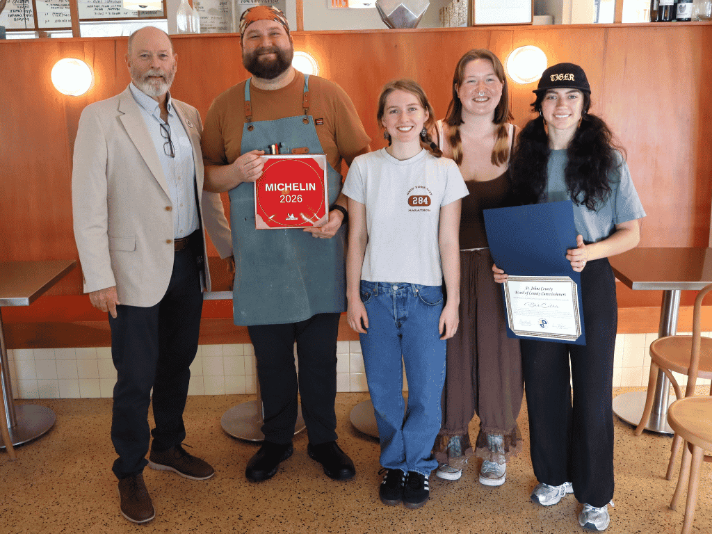 A group of five individuals pose for a photo in a restaurant setting, two holding certificates. One reads Michelin 2026.