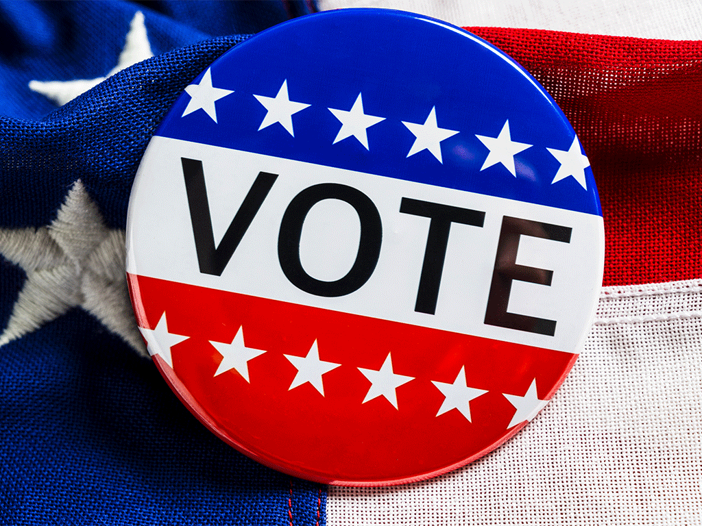 Red, white, and blue button with stars and text reading VOTE with an American flag as the background