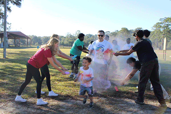 Two lines of volunteers fling colored powder onto smiling runners dashing in between them.