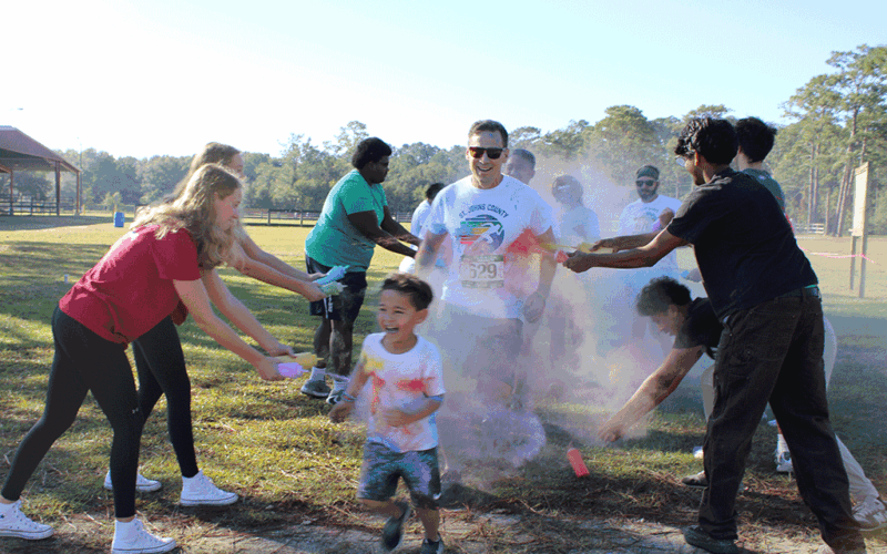 Two lines of volunteers fling colored powder onto smiling runners dashing in between them.
