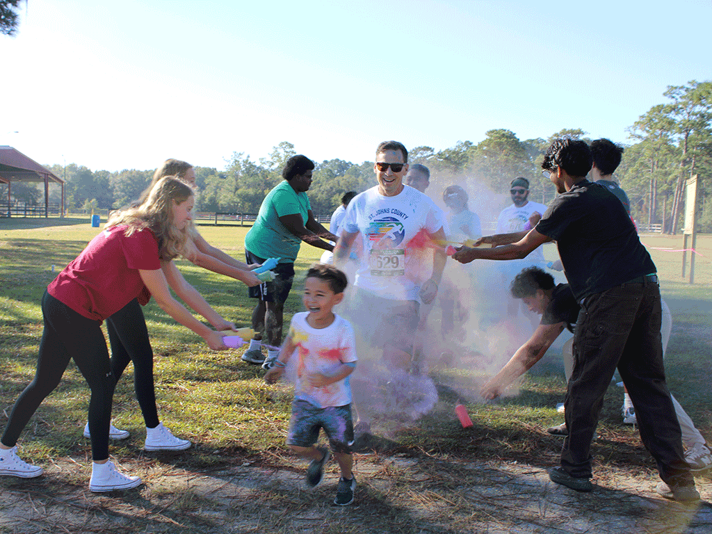 Two lines of volunteers fling colored powder onto smiling runners dashing in between them.