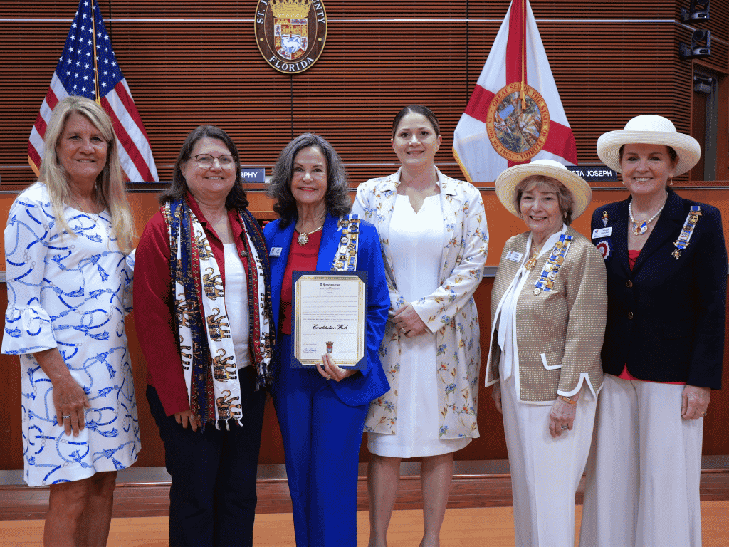 Individuals stand together, one holding a certificate, with the American Flag, Florida flag, and St. Johns County Seal in the background
